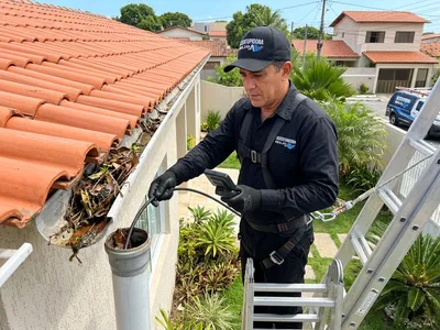 Técnico de uniforme preto desobstruindo a tubulação de uma calha